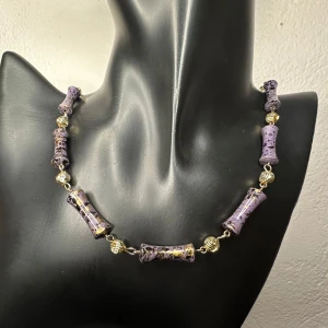 Lila och guldigt statement retrohalsband från 1980-talet Vintage Auktionsfynd Fint skick  -  Retrohalsband från 1980-talet med lila stavformade pärlor dekorerade med svart och guldstänk. Pärlorna är åtskilda av guldfärgade räfflade mellanpärlor som ger smycket ett konstnärligt och bohemiskt uttryck. Halsbandet är ca 90 cm långt och kan bäras både enkelt och dubbelvikt. Materialet är sannolikt äldre plast, men jag kan inte säga säkert. Fint vintageskick. Prutning accepteras inte, men jag ger rabatt vid köp av flera smycken och plagg. 