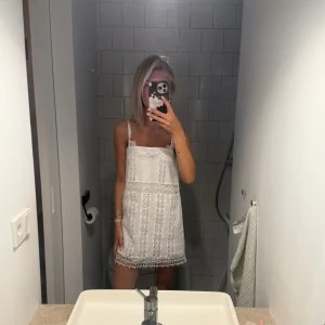 Vit spetsklänning med smala axelband - Superfin vit kortklänning med smala axelband och vackra spetsdetaljer. Klänningen har raka linjer och är ärmlös, perfekt för varma dagar. Snygg och enkel att styla med accessoarer för en trendig look.