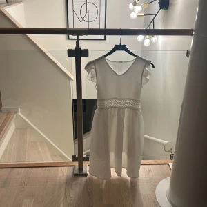 Vit kortklänning med spetsdetalj -  vit kortklänning med v-ringning, volangärmar och broderad spets.  