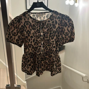Leopardmönstrad blus från Gina Tricot - blus från Gina Tricot med leopardmönster i beige och svart. Modellen har puffiga korta ärmar och volang nedtill.