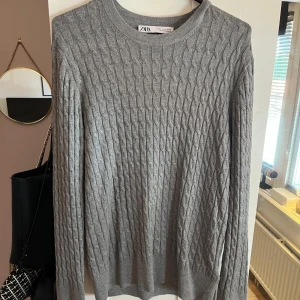Grå kabelstickad tröja från Zara - Säljer en grå kabelstickad tröja från Zara i storlek XL. Tröjan har rund halsringning, långärmade ärmar och ribbade muddar. Den har en tight passform. 
