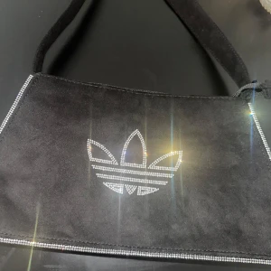 Adidas väska  - Oanvänd Adidas väska, med strass och i mocca imitation. Legat i garderoben, inte min stil men sjukt snygg! Fått i present därav säljer. Saknar etikett men är i skick som ny! Ordpris 799kr 