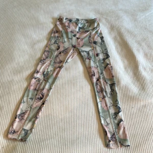 Blommiga leggings från SOC - Snygga leggings från SOC med blommigt mönster i pastelliga toner av grönt, rosa och beige. De är tighta och har hög midja, perfekta för träning eller chill. Materialet är stretchigt och mjukt för maximal komfort.