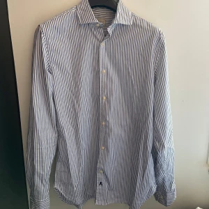 Blåvit randig skjorta från Scalpers - Snygg blåvit randig skjorta från Scalpers i klassisk modell. Skjortan har långa ärmar, knappar framtill och krage. Perfekt för dig som gillar stilrena och fräscha plagg. Tillverkad i mjuk bomull som känns skön mot huden.