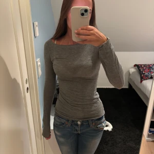 Grå långärmad slim tröja - Säljer en enkel och stilren grå långärmad tröja med tight passform. Tröjan har rund halsringning och är gjord i ett mjukt och stretchigt material som sitter snyggt på kroppen. Perfekt att matcha med jeans eller kjol för en clean look.