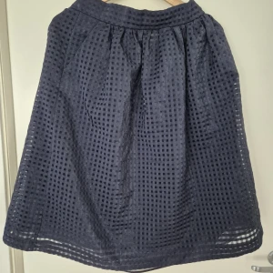 Mörkblå kjol från Bondelid, M - Supersnygg mörkblå kjol från Bondelid i modellen Vivianne. Kjolen har ett rutigt, transparent mönster och är lätt utställd med midjeresår. Perfekt för dig som gillar en klassisk men ändå trendig look.