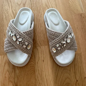 Beige sandaler med pärldetaljer - Snygga beige sandaler från XIT med breda, virkade band och glittrande pärldetaljer. Skorna har öppen tå och platt sula, perfekta för varma dagar. De stickade banden ger en cool och trendig look.