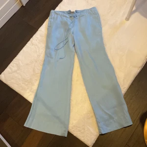 Ljusblå linnebyxor Calvin Klein Jeans - Snygga ljusblå linnebyxor från Calvin Klein Jeans med avslappnad passform och snörning i midjan. Byxorna är tillverkade i 100% linne och har raka, vida ben för en chill vibe. Perfekta för varma dagar när du vill vara både bekväm och stilren. Passar xs-s dam då midjan kan dras åt med snörena