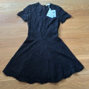 Svart spetsklänning Michael Kors - Supersnygg svart kortklänning från Michael Kors i spets med rund hals och korta ärmar. Klänningen har dragkedja bak och ett feminint, lätt utsvängt kjolparti. Perfekt för dig som vill ha en klassisk men trendig look. Oanvänd. Passar dig med 36/38. 