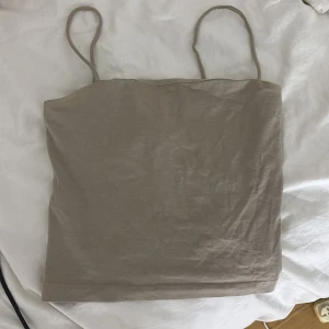 Beige linnetopp från Gina Tricot XS - Enkel och stilren beige linnetopp från Gina Tricot i storlek XS. Toppen har tunna axelband och rak skärning, perfekt för varma dagar. Mjuk och lätt i materialet, vilket gör den superbekväm att bära. Snygg att matcha med jeans eller kjol.