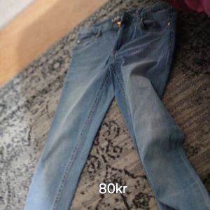 Blå jeans med smal passform - Säljer ett par klassiska blå jeans med smal passform. Jeansen har fem fickor, gylf med dragkedja och knapp samt snygga guldfärgade detaljer vid fickorna. Perfekta till sneakers eller boots.