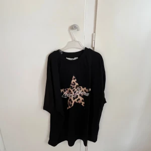 Svart oversized tröja med leopardstjärna - Svart oversized tröja med en stor stjärna i leopardmönster på bröstet och texten 'Love Roma' tryckt över stjärnan. Tröjan har rund halsringning och långa ärmar. Passar större storlekar.