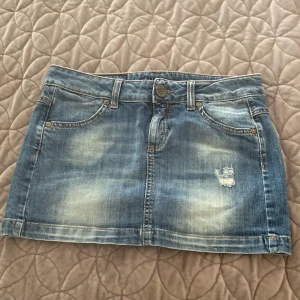 Blå mini jeanskjol från Sisley - Söt blå mini-jeanskjol från Sisley med slitningar framtill och coola bakfickor med dekorativa sömmar och nitar. Perfekt för dig som gillar kortare kjolar med en vintagelook. Ganska efterfrågad, pris kan diskuteras!