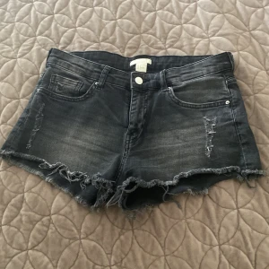 Svarta jeansshorts med slitningar H&M - Snygga svarta jeansshorts från H&M i storlek S, 36. De har fransiga benslut och slitna detaljer framtill. Perfekta för sommaren!🖤
