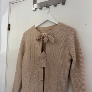 Beige stickad kofta med knyt från Pieces - Supermysig beige stickad kofta från Pieces med ribbad struktur och snygga knytband framtill. Långärmad och perfekt för lager-på-lager under höst och vinter. Enkel och stilren design som passar till allt.