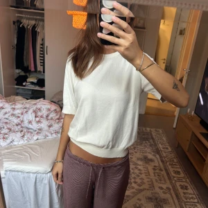 Vit kortärmad stickad tröja - Säljer en vit, kortärmad stickad tröja med rund hals och ribbade kanter. Tröjan har en relaxed passform och är perfekt för dig som gillar en enkel men stilren look. Passar lika bra till jeans som till kjol.