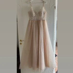 Cremefärgad balklänning  - Säljer nu min älskade balklänning som endast är använd en gång! Klänningen är cremefärgad med rosa/ beiga toner och har glittrig paljettöverdel med v-ringning. Kjolen är i flera lager tunn tyll som ger en prinsessform. Smala axelband och dragkedja i ryggen, samt inlägg för brösten så ingen bh behövs. Ryggen är djupt v- ringad vilket ger klänningen en fantastisk form. Köpt från Bubbleroom för 3000kr.(Är 176cm lång och längden är lagom, skulle passa någon upp till 180, går även sy upp för kortare)