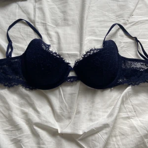 Mörkblå spetsig bh-topp - Snygg mörkblå bh-topp med vadderade kupor och vacker spetsdetalj över hela framsidan och banden. Spetsen har blommigt mönster och fina kanter som ger en extra touch. Justerbara axelband för perfekt passform.