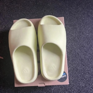 Adidas Yeezy tofflor/Slide i ljusgrön - Adidas Yeezy Slide i en fräsch ljusgrön färg. Slidesen har en chunky, minimalistisk design med öppen tå och platt sula. Tillverkade i mjukt syntetmaterial för maximal komfort. Perfekta för chill dagar eller när du vill sticka ut med en clean look. Säljs endast för 549