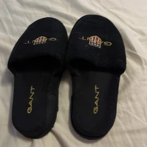 Svarta tofflor från Gant med brodyr - Mörkblåsvarta tofflor från Gant med broderad logga. Har använt dom cirka 3-5 gånger så it slitna 