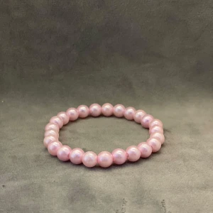 Rosa pärlarmband med glans - Snyggt armband med glansiga rosa pärlor på elastisk tråd. Perfekt accessoar för att ge din outfit en söt och trendig touch. Pärlorna är jämna och har en mjuk, ljusrosa färg som fångar ljuset fint.