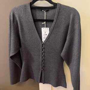 Grå kofta med v-ringning från Gina Tricot - Supersnygg kofta från Gina Tricot med djup v-ringning och klädda knappar framtill. Toppen har prislapp! Perfekt att styla med jeans eller kjol💓💓