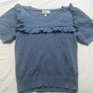 Blå stickad topp med volang & Other Stories - Supersöt blå stickad topp från & Other Stories med korta ärmar och volangdetalj över bröstet. Snyggt mönsterstickad struktur och rund halsringning. Perfekt för dig som gillar något gulligt men också klassiskt. .