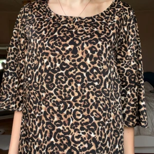 Leopardmönstrad blus från Ellos - Säljer en snygg blus från Ellos i storlek 38 med leopardmönster i brunt, svart och beige. Blusen har rund halsringning och trekvartsärmar. Perfekt för dig som vill sticka ut med ett djurmönstrat plagg!