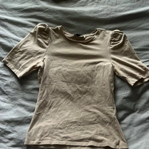 Beige topp med puffärm från Pigalle - Säljer en beige topp från Pigalle i storlek XS. Toppen har korta puffärmar och en rund halsringning. Enkel och stilren design som passar perfekt till jeans eller kjol. Mjuk och skön bomullskänsla. Kommer klippa bort lappen då det står mitt namn på den💕