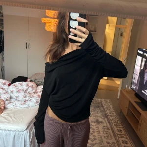 Svart offshoulder långärmad tröja - Svart långärmad tröja med offshoulder-look och snygg drapering bak, men man kan ha den åt båda hållen. Tröjan har en öppen rygg och sitter lite löst över axlarna för en chill vibe. Perfekt att styla med jeans eller kjol för en trendig look.