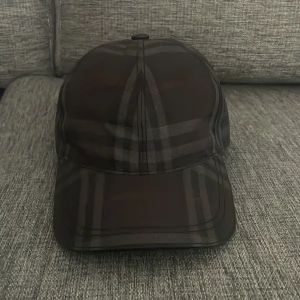 Svart rutig keps från Burberry - Snygg svart keps från Burberry med klassiskt rutigt mönster i mörka toner. Kepsen har justerbar rem Priset kan diskuteras! Använd fåtal gånger