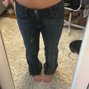 Blå bootcut jeans från Blue Fire - Snygga mörkblå jeans från Blue Fire med bootcut passform. Jeansen har klassiska fem fickor, kontrastsömmar i gult och orange samt knappstängning fram. Perfekta för dig som gillar en lite vidare siluett nertill. Materialet är klassisk denim.