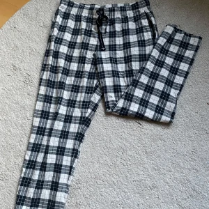 Rutiga pyjamasbyxor med snörning från Kappahl - Snygga och sköna rutiga pyjamasbyxor från Kappahl i svart och vitt. De har elastisk midja med snörning och raka ben. Perfekta för en chill och avslappnad stil. Tillverkade i mjukt bomullstyg som känns skönt mot huden.