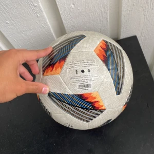 Adidas Tiro Pro elit fotboll - Säljer en Adidas Tiro Pro elit fotboll i storlek 5. Bollen är vit med coola grafiska detaljer i svart, blått och orange. Tillverkad i slitstarkt syntetmaterial och har en klassisk paneldesign med mönstrade ränder. Perfekt för matcher och träning.
