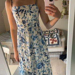 Blåvit blommig långklänning med smala axelband - Superfin långklänning med smala axelband och blått blommönster på vit botten. Klänningen har en figurnära överdel och utställd kjol, perfekt för sommarens varma dagar. Materialet känns lätt och luftigt. Den är endast använd en gång och därför i mycket bra skick 💋