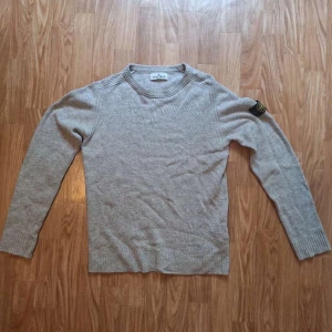 Grå stickad tröja Stone Island Junior - Snygg grå stickad tröja från Stone Island Junior med klassisk logga på ärmen. Passar 170cm. Mycket bra skick, inga fläckar eller defekter. Hör av dig vid minsta fundering eller fråga!