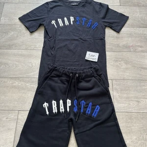 Svart Trapstar t-shirt med tryck - Svart t-shirt från Trapstar med stort broderat logotyp-tryck i vitt och blått över bröstet. Klassisk passform med rund hals och korta ärmar. Perfekt för dig som gillar streetwear och vill sticka ut med en fet logga.