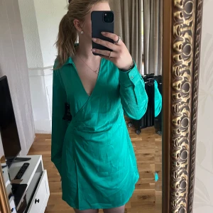 Grön omlottklänning med lång ärm - Snygg grön kort omlottklänning med v-ringning och långa ärmar från Na-kd. Aldrig använd, lappen sitter fortfarande kvar. Säljer då jag inte får användning för den. Hör av dig vid frågor, pris går att diskutera🫶