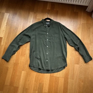 Grön skjorta från East West, storlek L - Stilren grön skjorta från East West i storlek L. Skjortan har klassisk krage, bröstficka och vita knappar framtill. Långärmad modell med enkel, clean design. Använd max 1 gång så den är i väldigt fint skick! Pris kan diskuteras 💫