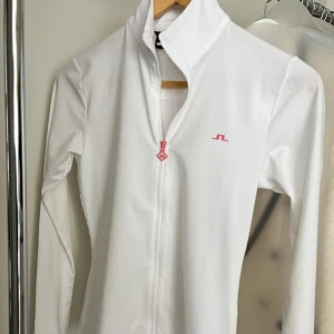 Vit golftröja från J.Lindeberg - I fin skick. Normal i storlek och lite åtsittande i midjan.