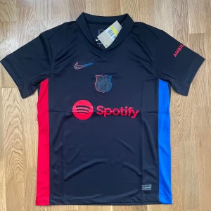 🖤 FC Barcelona Bortatröja 2024/25 – Storlek S 🖤 - Säljer en ny och oanvänd FC Barcelona bortatröja för säsongen 2024/2025. ⚽ Storlek: Small (S) 🖤 Svart med rödblå detaljer och Spotify-logga 🔥 Stilren och modern design 👌 Aldrig använd – endast uppackad för bild