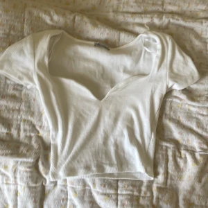 Vit ribbad croppad topp från Zara - Säljer en vit croppad topp från Zara med v-ringning och korta ärmar. Toppen är ribbad och har en figurnära passform som framhäver siluetten. Perfekt att matcha med jeans eller kjol för en clean look.