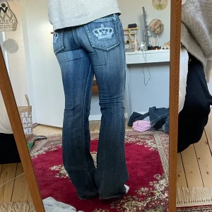 Victoria Beckham bootcut jeans - Snygga blå bootcut jeans från Victoria Beckham x Rock & Republic med ikonisk kronbrodyr på bakfickorna. Jeansen har låg midja, klassisk femficksdesign för en snygg look. Står ingen storlek på jeansen, ungefär xs (kontakta för mått) 