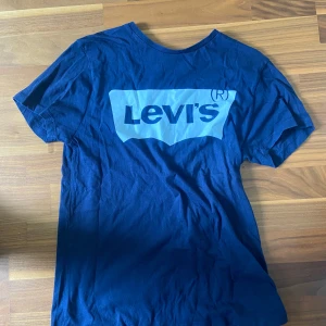 Blå Levi's t-shirt med logga - Snygg blå t-shirt från Levi's med stor ljusblå logga framtill. Klassisk rund halsringning och korta ärmar. Perfekt för dig som gillar streetstyle och vill ha en enkel men ikonisk look. Tillverkad i mjuk bomull för skön känsla hela dagen.