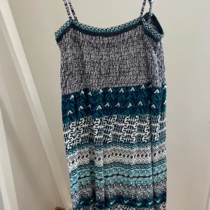 Mönstrad sommarklänning från Indiska - Säljer en luftig långklänning från Indiska med tunna axelband. Klänningen har ett coolt mönster i blått, vitt och svart med olika grafiska ränder och detaljer. Perfekt för varma dagar och stranddagar.