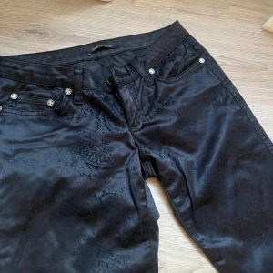 Svarta lågmidjade paisleymönstrade byxor Roberto Cavalli - Snygga svarta super lågmidjade byxor från Roberto Cavalli med diskret paisleymönster i tyget. Byxorna har raka ben och är extremt lågmidjade men leopardfickor. Står ej storlek men gissar på XXS/XS