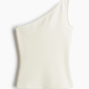 Vit one shoulder topp i S - Snygg vit one shoulder topp med smal axelrem på ena sidan. Toppens stilrena design gör den lätt att matcha och den är sydd i ett mjukt, lätt material som känns skönt mot huden. Perfekt för dig som gillar minimalistiska plagg med en twist.