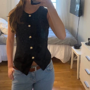 Svart tröja med guldknappar - Snygg svart tröja  med markerad midja och spetsig nederkant. Tröjan har fem stora guldknappar framtill som ger en elegant look.