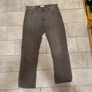 Grå jeans från Jack & Jones - Säljer ett par grå jeans från Jack & Jones med en relaxed passform. Byxorna har en klassisk fyrficksdesign och är tillverkade i bomull. Perfekta för en avslappnad stil.