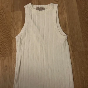 Vit ribbad ärmlös topp - Säljer en stilren vit ribbad topp utan ärmar. Perfekt för varma dagar eller som ett lager under en jacka. Toppen har en enkel och klassisk design som passar till det mesta.